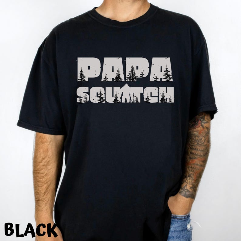 May include: Black t-shirt with a white graphic print that says "Papa Squatch" with a stylized image of a Bigfoot and trees.