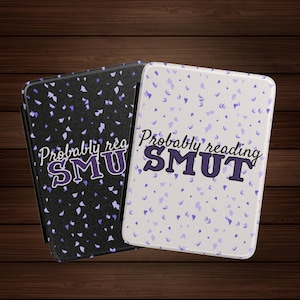May include: Two rectangular phone cases with the text "Probably reading SMUT". One case is black with purple confetti, the other is white with purple confetti. The text is in a purple, stylized font.