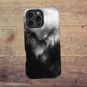 May include: A black and white phone case featuring a dragon soaring over a misty forest. The design is detailed, with the dragon's wings spread wide and the trees silhouetted against a bright sky. The case has a glossy finish.