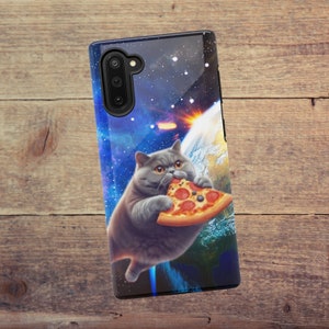 May include: A galaxy-themed phone case with a gray cat eating a pizza in front of a planet. The case has a black camera cutout and a black border.
