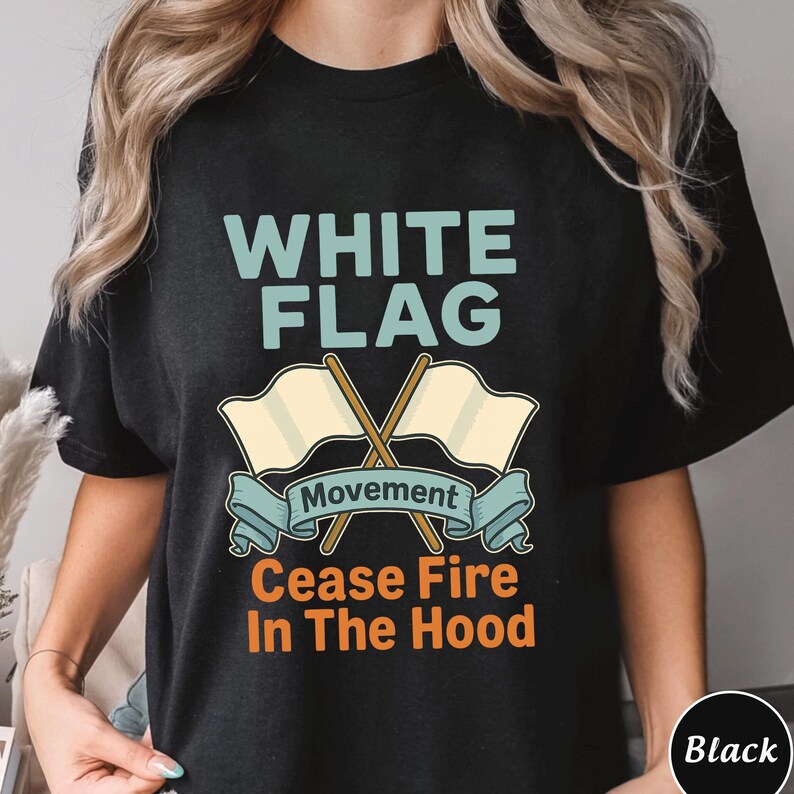 May include: Black t-shirt with a graphic design. The design features the words "WHITE FLAG" in light blue, above two crossed flags. Below the flags is the word "Movement" on a teal banner, and the words "Cease Fire In The Hood" in orange.