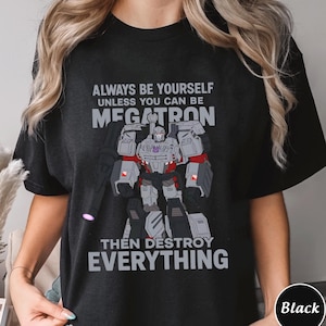 May include: Black t-shirt with a cartoon illustration of Megatron from Transformers. The design includes the text "ALWAYS BE YOURSELF UNLESS YOU CAN BE MEGATRON THEN DESTROY EVERYTHING". The graphic is in grey, red, and white.