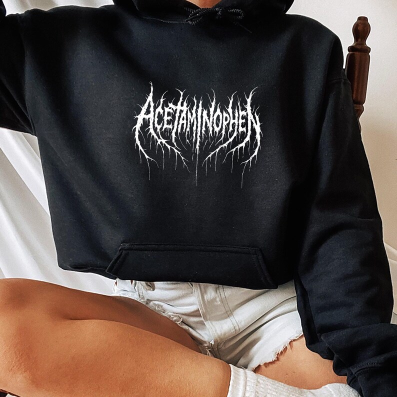 Puede incluir: Sudadera negra con bolsillo frontal y gr&aacute;fico blanco estilizado "Acetaminophen". El texto tiene una fuente g&oacute;tica y puntiaguda. La sudadera con capucha tiene una capucha con cord&oacute;n y un ajuste relajado.