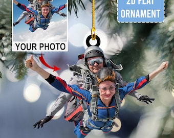 Può includere: Un addobbo natalizio piatto in 2D con una foto di due persone che fanno paracadutismo. L'addobbo ha la forma di un cerchio ed è dotato di un filo dorato per appenderlo. Il testo "YOUR PHOTO" è stampato sull'addobbo.