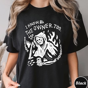 Peut inclure: T-shirt noir avec un graphique blanc d'un squelette dans une robe à capuche tenant une canette et une faux. Le texte "I know the owner, too." est imprimé sur le t-shirt.