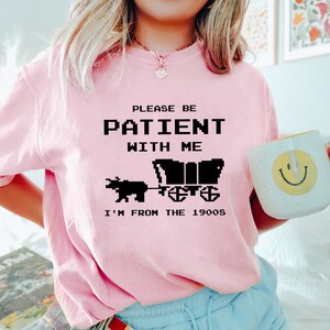 May include: Pink t-shirt with a black graphic that says "Please be patient with me I'm from the 1900s". The graphic is a pixelated image of a horse-drawn wagon.