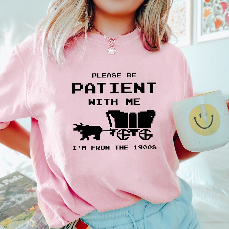 May include: Pink t-shirt with a black graphic that says "Please be patient with me I'm from the 1900s". The graphic is a pixelated image of a horse-drawn wagon.