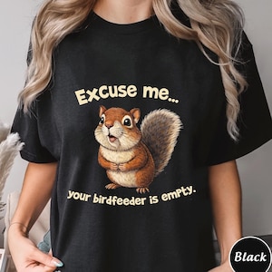 May include: Black t-shirt with a cartoon squirrel and the text "Excuse me... your birdfeeder is empty." The squirrel is brown, tan, and white with a fluffy tail. The text is in a playful font.