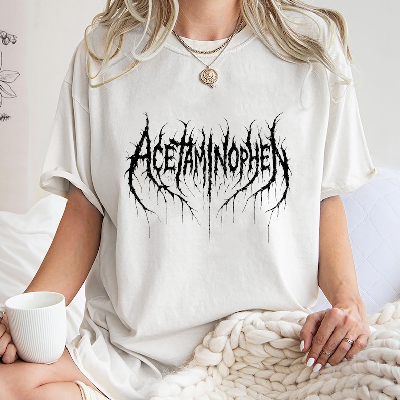 Puede incluir: Camiseta color crema con la palabra "ACETAMINOPHEN" en una fuente g&oacute;tica negra. El dise&ntilde;o tiene un aspecto desgastado y texturizado. La camiseta es de corte holgado y de gran tama&ntilde;o.