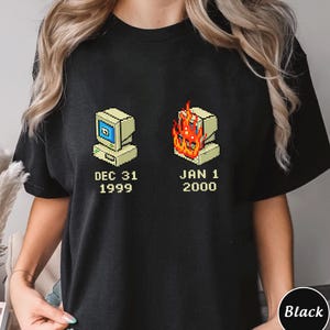 May include: Black t-shirt featuring a pixelated computer graphic. One computer shows a screen, the other is on fire. The text reads "DEC 31 1999" and "JAN 1 2000".