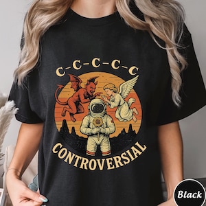 May include: Black t-shirt with a graphic design featuring an astronaut holding a sunflower, flanked by a devil and an angel. The word "CONTROVERSIAL" is printed below the astronaut, with "C-C-C-C-C" above. The shirt is a crew neck.