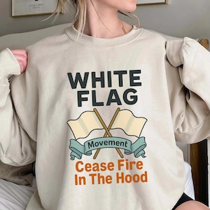 May include: Beige sweatshirt with the text "WHITE FLAG" above a graphic of two crossed flags and a banner that reads "Movement". Below the banner, the text reads "Cease Fire In The Hood".