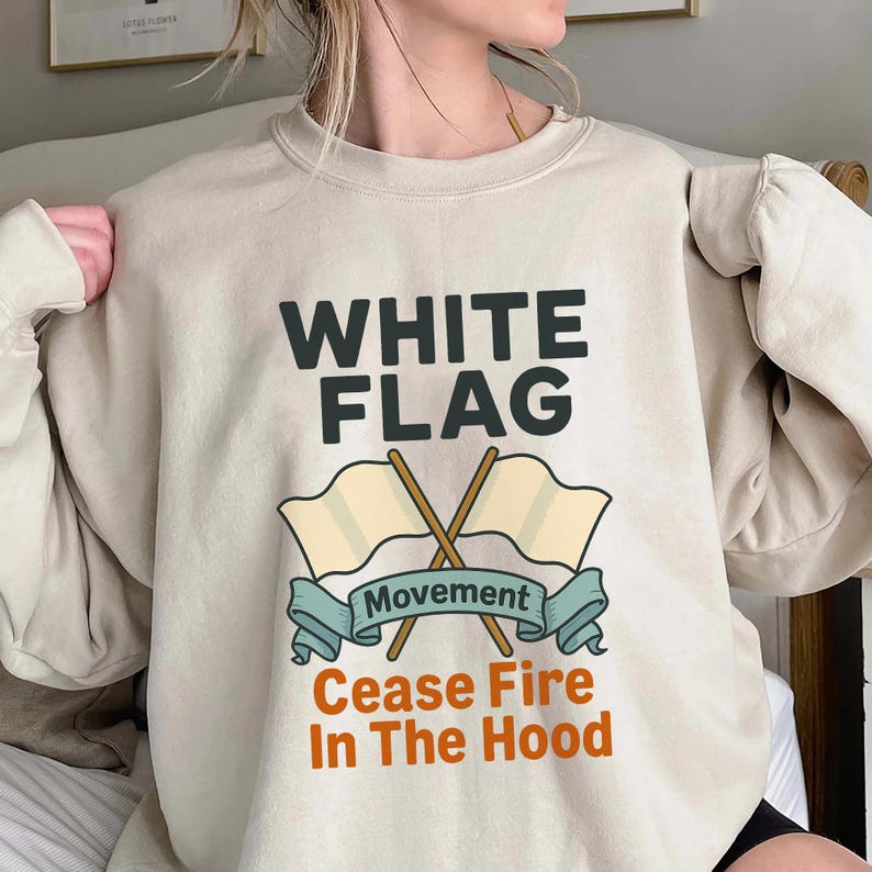 May include: Beige sweatshirt with the text "WHITE FLAG" above a graphic of two crossed flags and a banner that reads "Movement". Below the banner, the text reads "Cease Fire In The Hood".