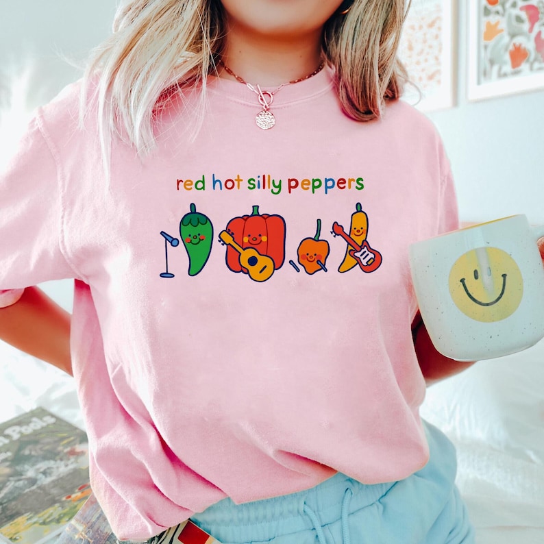 Pu&ograve; includere: Maglietta rosa con il testo "red hot silly peppers" e un'illustrazione di cartoni animati di peperoni che suonano musica.