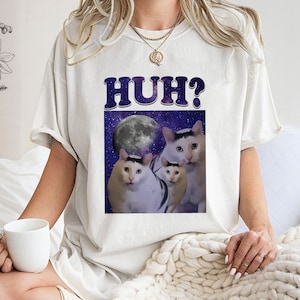 May include: White t-shirt with a graphic of three cats in space with a full moon. The text "HUH?" is printed in large, bold letters above the graphic.