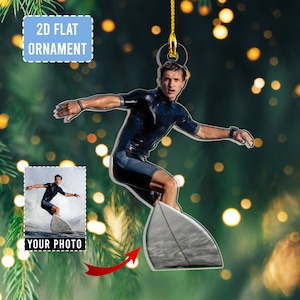 May include: A 2D flat ornament featuring a surfer in a black wetsuit riding a surfboard. The ornament has a gold string for hanging. The words "2D FLAT ORNAMENT" are in a blue rectangle. The words "YOUR PHOTO" are in a white rectangle.