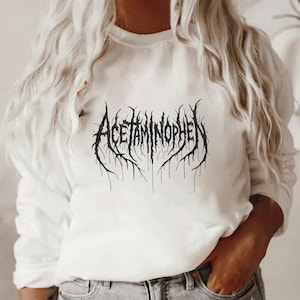 May include: White sweatshirt with the word "ACETAMINOPHEN" in a black, gothic-style font. The text has a distressed, textured appearance, with a design that resembles roots or branches.