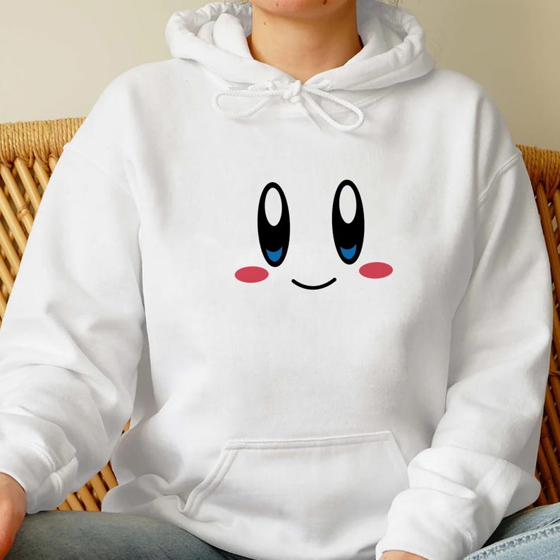 May include: White hooded sweatshirt featuring a cartoon face with large black eyes, blue pupils, and pink cheeks. The design is centered on the front of the hoodie. The sweatshirt has a drawstring hood and a front pocket.