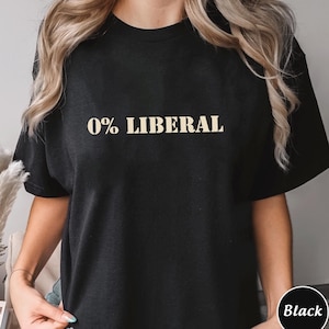 May include: Black t-shirt featuring the text "0% LIBERAL" in a tan, bold font. The shirt is a short-sleeved crew neck style. The image shows the shirt on a person.