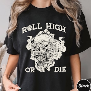 Könnte beinhalten: Schwarzes T-Shirt mit einem weißen Grafikdruck eines Schädels, der einen 20-seitigen Würfel hält. Der Text "Roll High or Die" ist über dem Schädel gedruckt.