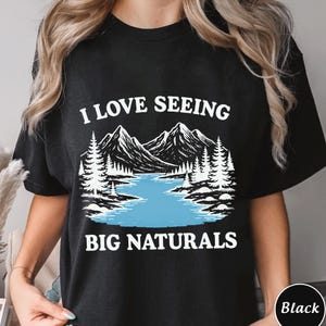 May include: Black t-shirt with the text "I LOVE SEEING BIG NATURALS" in white. The graphic features a mountain range, lake, and pine trees in a black and white illustration with a blue lake.