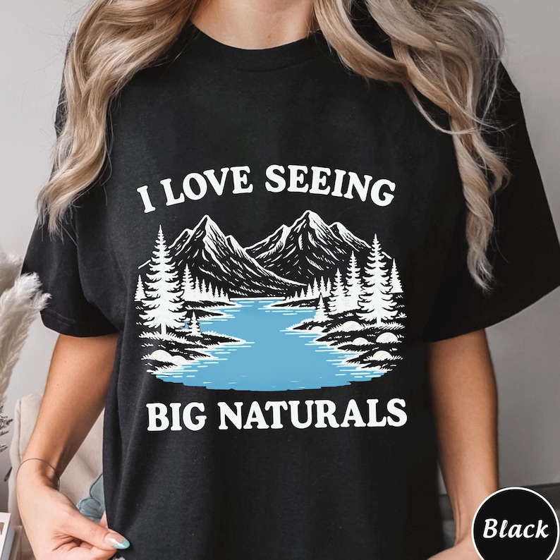 May include: Black t-shirt with the text "I LOVE SEEING BIG NATURALS" in white. The graphic features a mountain range, lake, and pine trees in a black and white illustration with a blue lake.