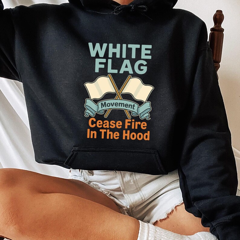 May include: Black hoodie with the text "WHITE FLAG" above crossed flags and the words "Movement Cease Fire In The Hood". The design features light blue, beige, and orange colors.