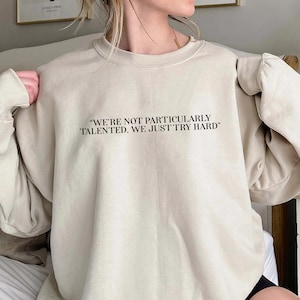 May include: A beige sweatshirt with the text "We're not particularly talented, we just try hard" printed on the front.