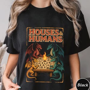 May include: Black t-shirt with a vintage-style graphic of three dragons playing a board game. The graphic says "Houses & Humans".