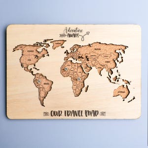 May include: Wooden world map with engraved continents and cork-filled countries. The map features the text "Adventure Awaits" and "Our Travel Map". Includes pin locations for travel memories.