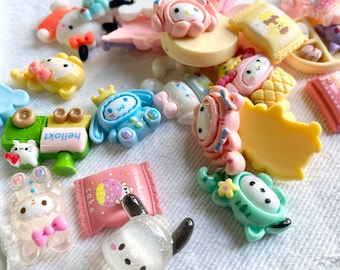 May include: A collection of colorful, small, decorative resin charms. The charms feature various designs, including cartoon characters, food items, and other cute shapes. The color palette includes pink, blue, yellow, and white. These charms are ideal for crafting and embellishment.