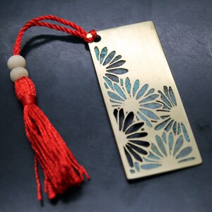 May include: A brass bookmark with a red tassel. The bookmark features a cut-out design of blue and black flowers.