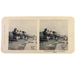 Może przedstawiać: Zabytkowa stereografia czarno-biała przedstawiająca pociąg ziemny w Canal Cut w Las Cascadas, Panama. Obraz przedstawia lokomotywę parową na torach z ludźmi w pobliżu. Fotografia jest zamontowana na kartonowym podkładzie.