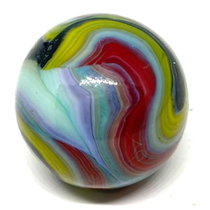 May include: A spherical glass marble featuring a swirling, multi-colored pattern. The surface displays vibrant streaks of red, bright yellow, light blue, lavender, and black, creating a marbled effect with a smooth, reflective, and glossy finish.