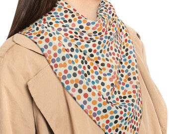 May include: A woman wearing a beige trench coat with a colorful polka dot scarf around her neck. The scarf is cream colored with blue, red, orange, and yellow polka dots.