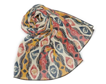 May include: A lightweight scarf featuring a repeating diamond and oval pattern in shades of red, yellow, blue, and black on an off-white background. The fabric has a semi-sheer appearance with a delicate black stitched edge along the hemline.
