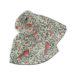 May include: A rolled scarf with a cream background featuring a pattern of red cardinals, red flowers, and green leaves. The scarf has a black trim along the edges, and the design is repeated across the fabric.