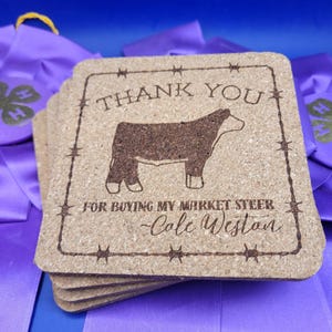 May include: A stack of brown cork coasters with a laser-engraved design. The design features a steer silhouette, the text "THANK YOU", and the message "FOR BUYING MY MARKET STEER -Cole Weston".