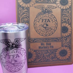 May include: A stainless steel tumbler and a brown leather-bound notebook. Both items feature the FFA emblem with an eagle, owl, and text. The notebook has sunflower and scrollwork designs. The tumbler has a clear lid.