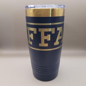 May include: Navy blue insulated tumbler with a gold rim and the letters "FFA" in gold. The tumbler has a clear lid and a gold band around the middle. The bottom of the tumbler has three horizontal grooves.