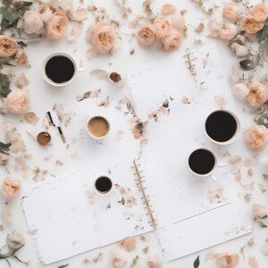 May include: A white spiral-bound planner with floral patterns, four white ceramic mugs filled with black coffee, and a gold-accented pen, all surrounded by scattered pale peach-colored rose blossoms and petals on a white surface.