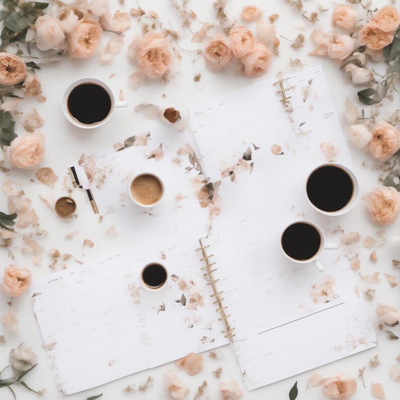 May include: A white spiral-bound planner with floral patterns, four white ceramic mugs filled with black coffee, and a gold-accented pen, all surrounded by scattered pale peach-colored rose blossoms and petals on a white surface.