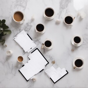 Puede incluir: Una colección de ocho tazas de café de cerámica blanca llenas de café negro o marrón claro, dispuestas junto a tres agendas de encuadernación negra con páginas blancas, sobre una superficie de mármol blanco con una pequeña planta verde.
