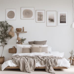 May include: A low-profile wooden bed frame with white bedding and a beige throw blanket. The bed is adorned with several beige and brown pillows. Above the bed, five framed abstract art prints are displayed on a white wall near a hanging lamp.