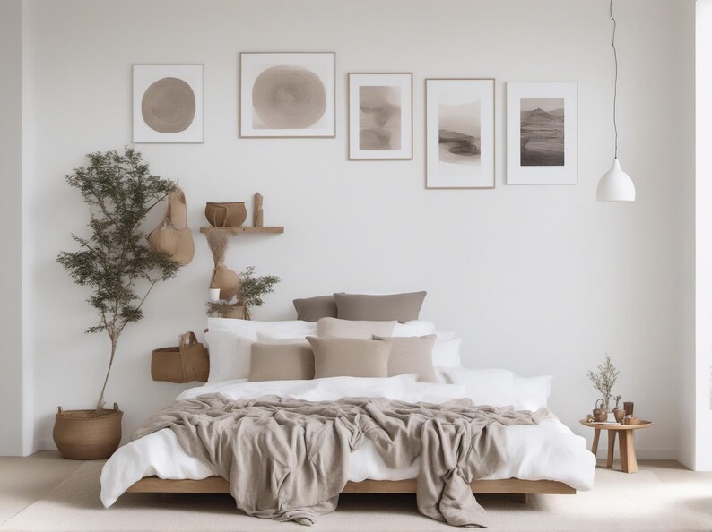 May include: A low-profile wooden bed frame with white bedding and a beige throw blanket. The bed is adorned with several beige and brown pillows. Above the bed, five framed abstract art prints are displayed on a white wall near a hanging lamp.