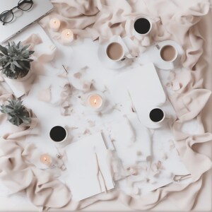 May include: A flat lay composition featuring a white surface surrounded by beige fabric, including four coffee cups, three lit candles, two small potted succulents, a pair of black-rimmed glasses, and several blank white paper sheets.