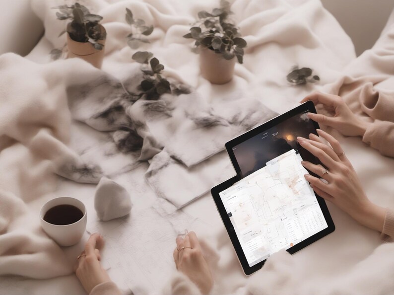 May include: Two black tablets with illuminated screens displaying digital maps and interface elements, positioned alongside a white ceramic cup filled with dark liquid and two small potted green plants on a soft, textured cream-coloured fabric.