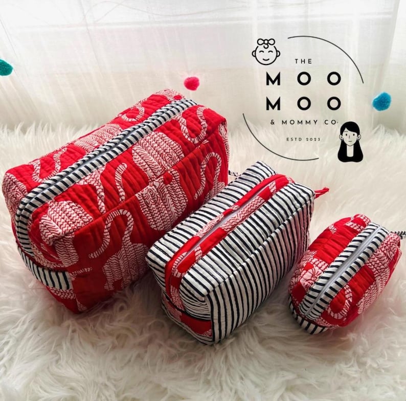 May include: Set of three red and white patterned cosmetic bags with black and white striped accents. The bags have zippers and are in varying sizes. The text "THE MOO MOO & MOMMY CO. ESTD 2013" is visible.