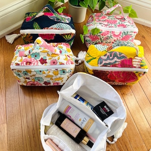 May include: Five colorful quilted fabric zippered pouches with a tassel. One pouch is open and filled with toiletries, including a bottle of Dove shampoo, a bottle of hand sanitizer, and a package of makeup wipes.