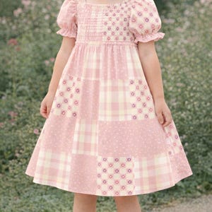 Könnte beinhalten: Ein rosa Patchwork-Kleid mit quadratischem Ausschnitt und kurzen Puffärmeln. Das Kleid hat ein gerafftes Oberteil und einen Rock mit verschiedenen Mustern, darunter Punkte, Blumendrucke und Karos. Das Kleid ist für ein Kind.